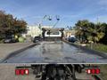 A 2022 Freightliner M2 106 flatbed truck with a metallic surface and red rear lights positioned in a clear area