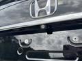 A rear view camera mounted below the logo of a 2014 Honda CR-V with a chrome trim and visible license plate holder screws