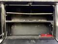 An empty black storage compartment with a metal shelf and a small red fire extinguisher positioned at the bottom