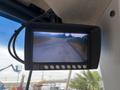 Screen display showing a rearview camera feed from a Caterpillar 980, depicting a curved road lined with trees and grass
