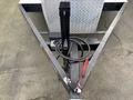 A black metal trailer hitch with a curved arm and a coiled wire attached, mounted on a diamond plate surface