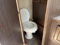 A white toilet is positioned in a small enclosed space with wooden paneling and a simple countertop nearby
