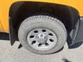 A silver wheel with five circular cutouts and a Chevrolet emblem mounted on a tire with visible tread patterns from a 2013 Chevrolet Silverado 1500