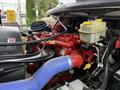 Engine compartment of a 2021 Freightliner M2 106 featuring a red engine, blue hose, and various components including a yellow cap reservoir and wiring