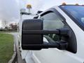 A close-up of the side mirror of a white 2008 Ford F-450 truck with orange lights on the roof and a silver body near the rear
