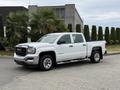 A white 2016 GMC Sierra 1500 pickup truck with chrome accents and a crew cab parked on a driveway with palm trees nearby