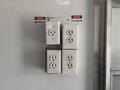 A panel with four electrical outlets labeled with warning signs for 220 volts and 115 volts