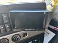 A black, rectangular dashboard display unit with buttons and controls situated above various gauges and dials in a vehicle's interior