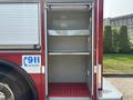 A 1999 Freightliner FL80 with an empty storage compartment featuring metal shelves and a red rubber floor mat