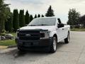 A white 2018 Ford F-150 pickup truck with a black grille parked on a driveway with a single cab and silver wheels