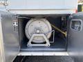 A large silver cylindrical tank secured on a bracket inside a storage compartment with a yellow hose attached