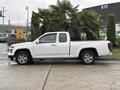 A white 2011 Chevrolet Colorado pickup truck with a standard cab and chrome accents parked beside green plants