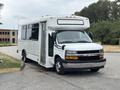 A white 2020 Chevrolet Express with a large side door, designed for passenger transport, featuring a black front grille and chrome accents