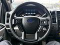 A 2015 Ford F-150 steering wheel featuring controls for audio and cruise settings with the Ford logo in the center