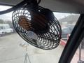 A small metal desk fan mounted inside a vehicle, with visible blades and a circular protective grille