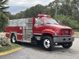 A red 2002 GMC C7500 firetruck with emergency lights and a water pump system on the side