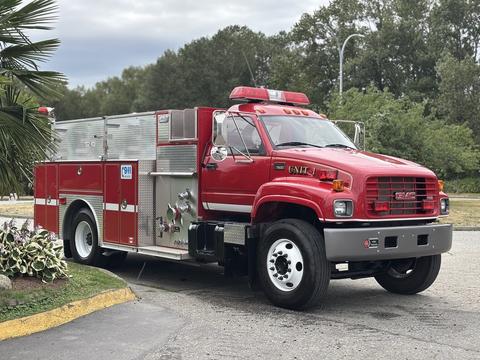 A red 2002 GMC C7500 firetruck with emergency lights and a water pump system on the side