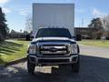 A 2010 Ford F-450 parked with a white box truck attached to the back facing forward with its headlights on and a chrome grille visible