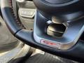 Close-up of a steering wheel featuring a silver GT emblem and red stitching on a black leather surface