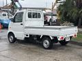A white 2010 Suzuki Carry mini truck with an open cargo bed and a cab that seats two people