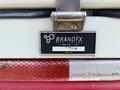 A metal nameplate from BrandFX Body Company mounted on a vehicle with a red and white chevron pattern