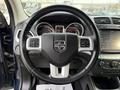 Steering wheel of a 2013 Dodge Journey featuring the Dodge logo and control buttons with a dashboard display behind it