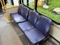 A row of four blue upholstered seats inside a bus with a smooth gray floor and visible seating arrangement