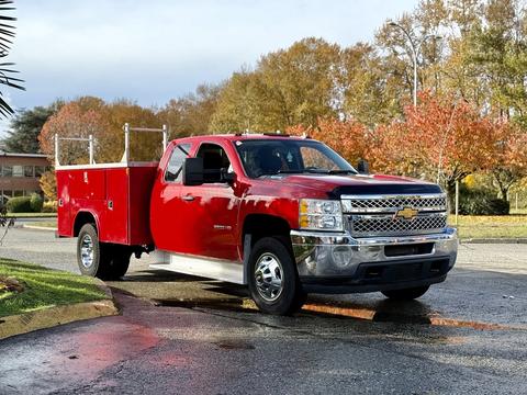 A red 2013 Chevrolet Silverado 3500HD pickup truck with an open utility bed is parked on a street showcasing chrome accents and a large front grille