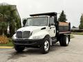 A 2006 International 4200 truck with a dump bed in the back painted black and white with six wheels and amber lights on the roof