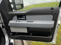 Interior door panel of a 2014 Ford F-150 featuring a gray armrest and controls for windows with a small storage compartment at the bottom