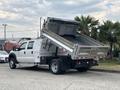 A 2014 Ford F-550 dump truck with its bed raised, revealing a steel dumping compartment in the rear, parked on a concrete surface