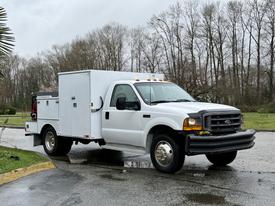 A 2000 Ford F-450 utility truck in white with a service body and black grill parked on a wet surface