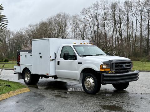A 2000 Ford F-450 utility truck in white with a service body and black grill parked on a wet surface