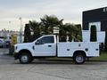 A white 2018 Ford F-350 truck with a flatbed and side compartments parked beside greenery