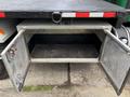 A metal storage compartment with two hinged doors on a flatbed truck showing a clean interior and a textured surface on the top