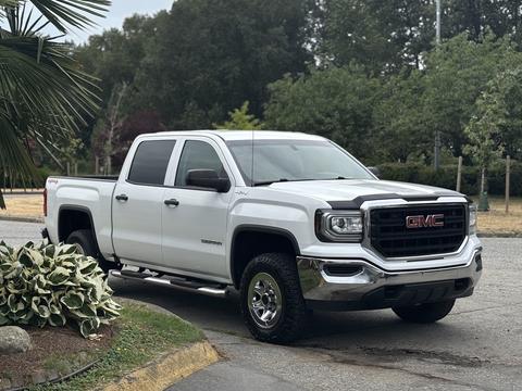 A 2016 GMC Sierra 1500 in white with chrome accents parked on a driveway featuring a large front grill and four-door crew cab design