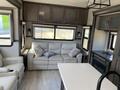 A 2021 Grand Design Recreational ST3478MBS interior featuring a light-colored sofa with cushions a kitchenette area and a cozy fireplace setup