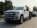 A white 2021 Ford F-350 Super Duty pickup truck with a flatbed is parked on the side of the road