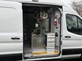 A 2023 Ford Transit van with its side door open revealing a specialized interior equipped with shelving and various equipment for work purposes