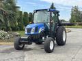 A blue and black 2009 New Holland T4020 tractor with a front loader and large rear tires is positioned prominently in the foreground