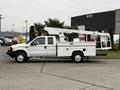 A white 2001 Ford F-350 with an extended cab and utility service body, equipped with a yellow light bar and a lift bucket on the rear for maintenance work