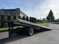A 2022 Freightliner M2 106 flatbed truck with a long, lowered ramp in the foreground