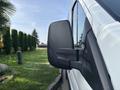 A side mirror of a 2016 Ford Transit 150 reflecting the surrounding greenery and sunlight