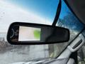 A rearview mirror displaying a backup camera feed with a view of a driveway and green grass