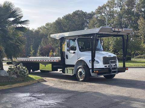 A 2022 Freightliner M2 106 flatbed truck with a white body and a silver flatbed visible in the foreground