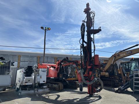 A 2018 Sandvik Ranger DX800 drilling rig with a tall red vertical mast and various hoses and cables attached to its structure