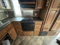 Interior view of a kitchen in a 2013 Outdoor Wind River featuring a black stovetop with oven beneath and wooden cabinetry surrounding it