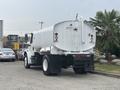 A 2006 Freightliner M2 106 truck with a white tank in the rear and large black tires parked in a lot