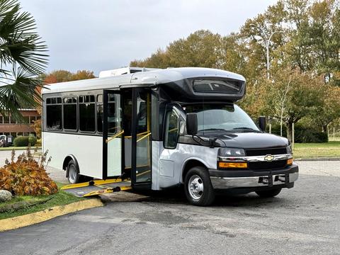 A 2019 Chevrolet Express bus with a black and white exterior featuring an open door and a ramp for accessibility