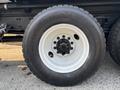 A close-up view of a black tire mounted on a white rim belonging to a 2016 Freightliner M2 106 truck featuring a five-bolt pattern and deep tread for enhanced traction